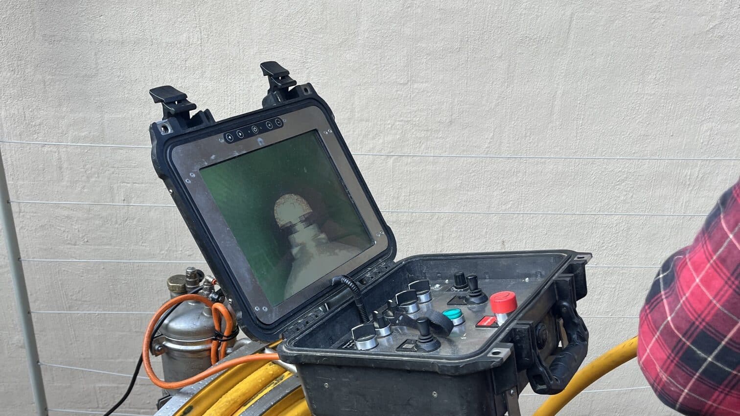 A drain camera reel and monitor showing the inside of a pipe during an inspection