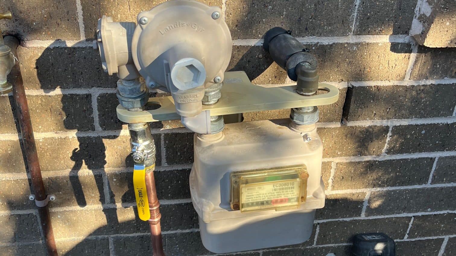 A domestic gas meter and regulator with a newly run copper gas line and yellow gas-marking tape