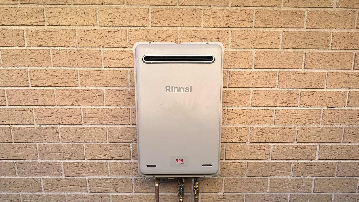 A Rinnai continuous-flow gas hot water unit installed on a brick wall with new copper pipework