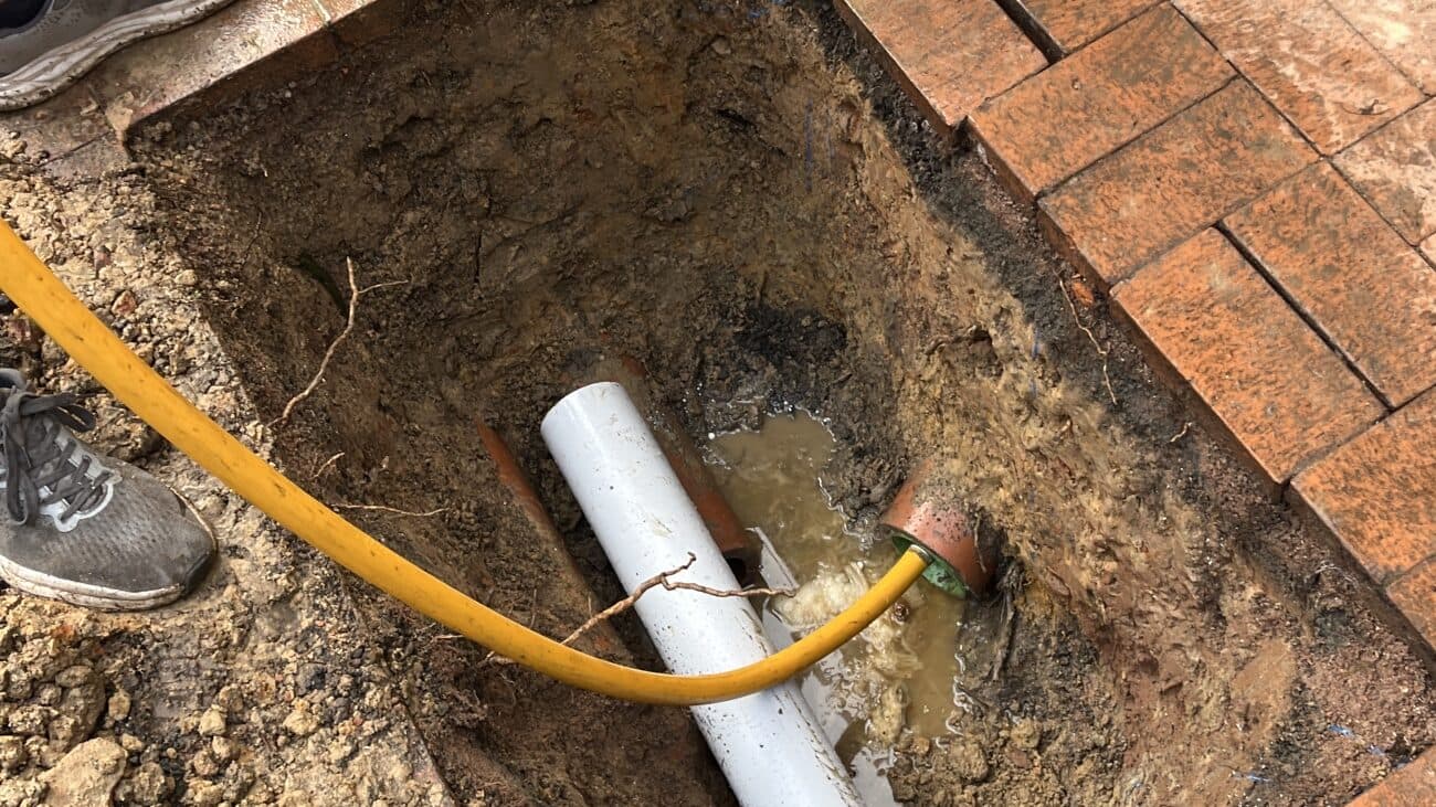 A relining hose being fed into an exposed clay drain pipe in an excavated trench