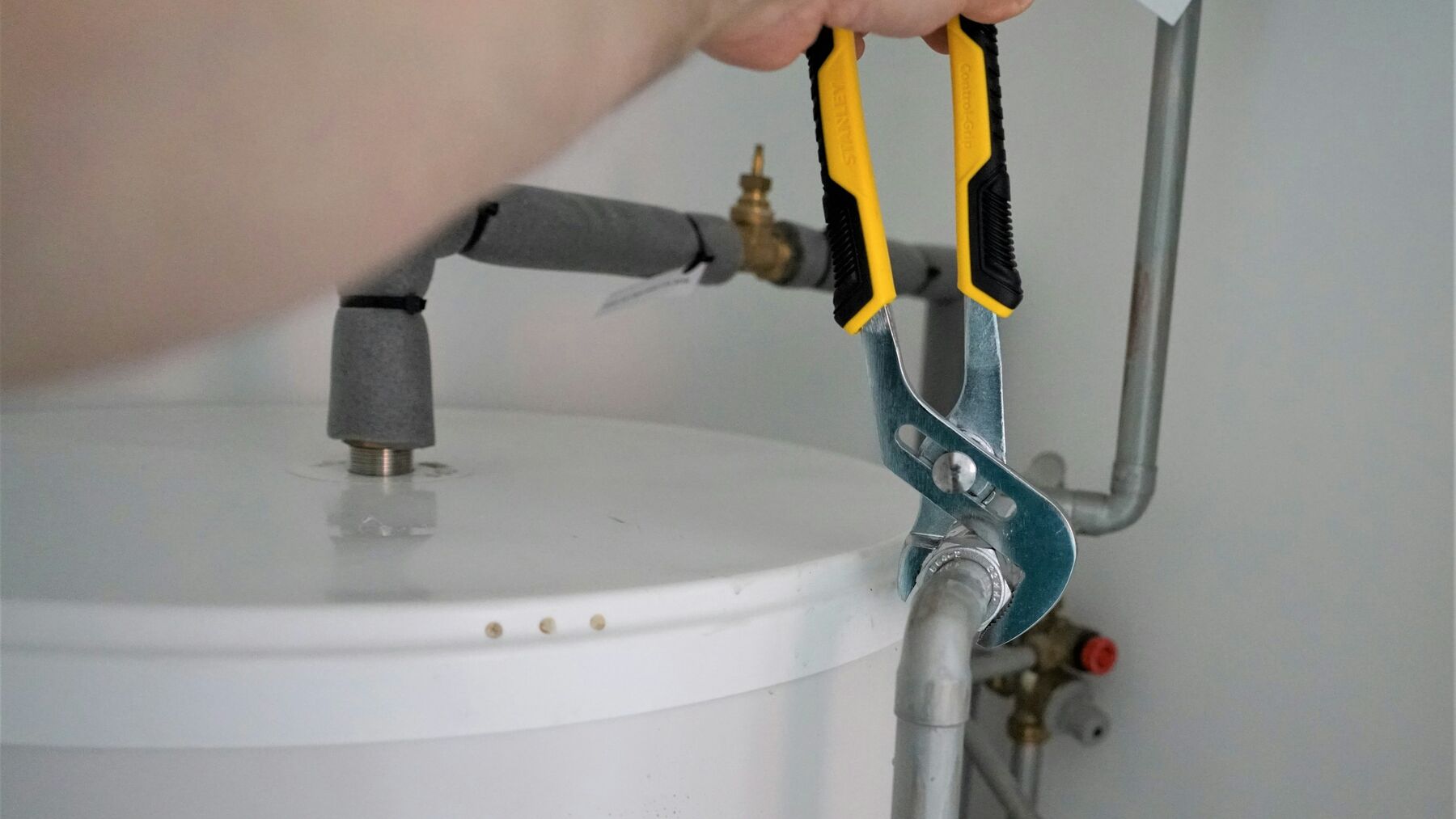A plumber tightening the pipe fittings on top of an electric hot water tank with a wrench