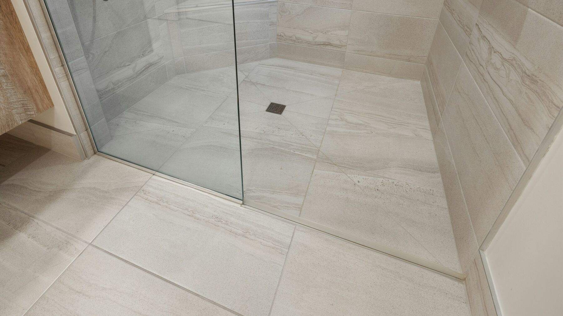 A walk-in shower with a glass screen and a drain in the tiled floor