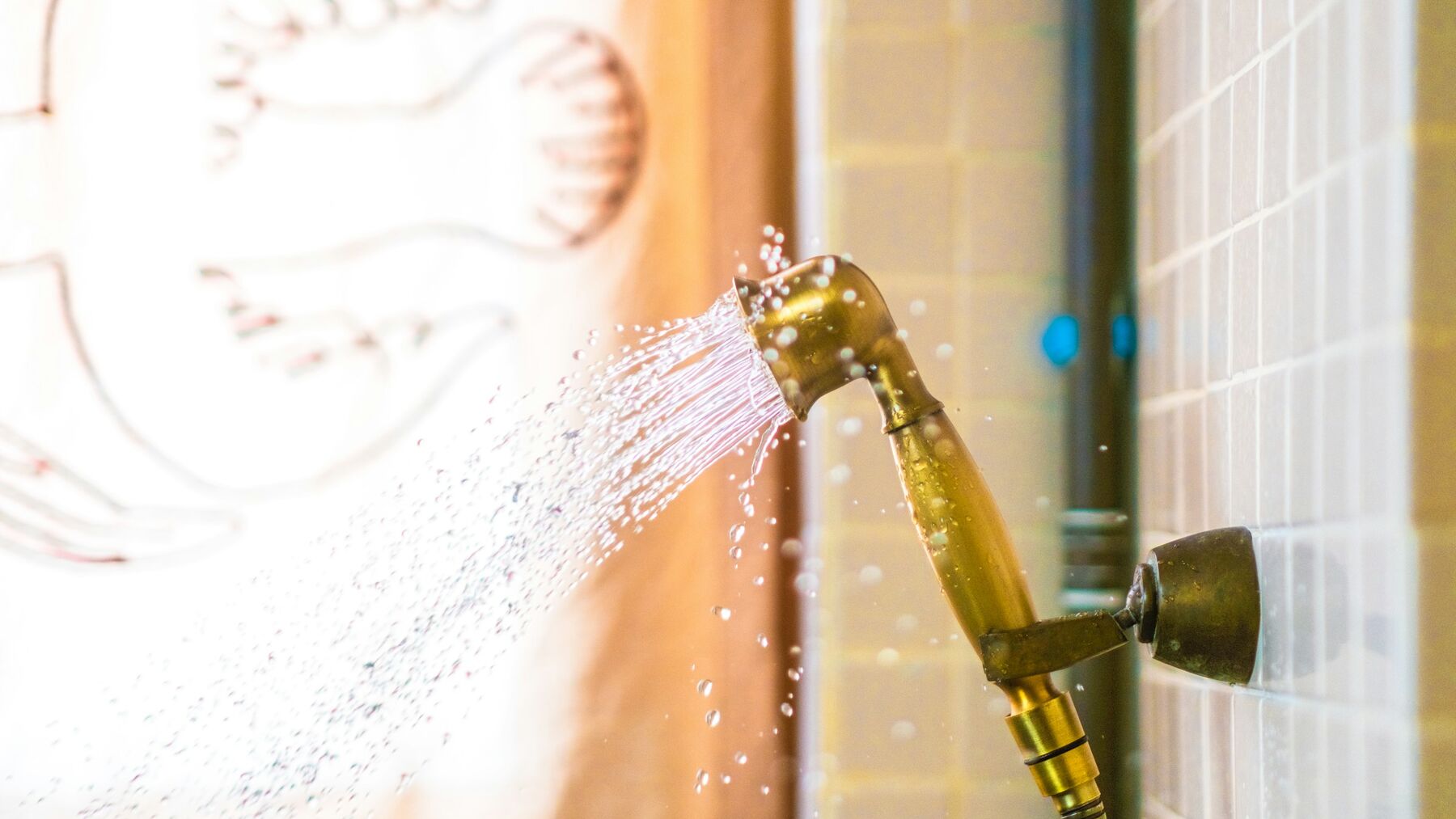 A brass hand shower spraying water against a tiled shower wall
