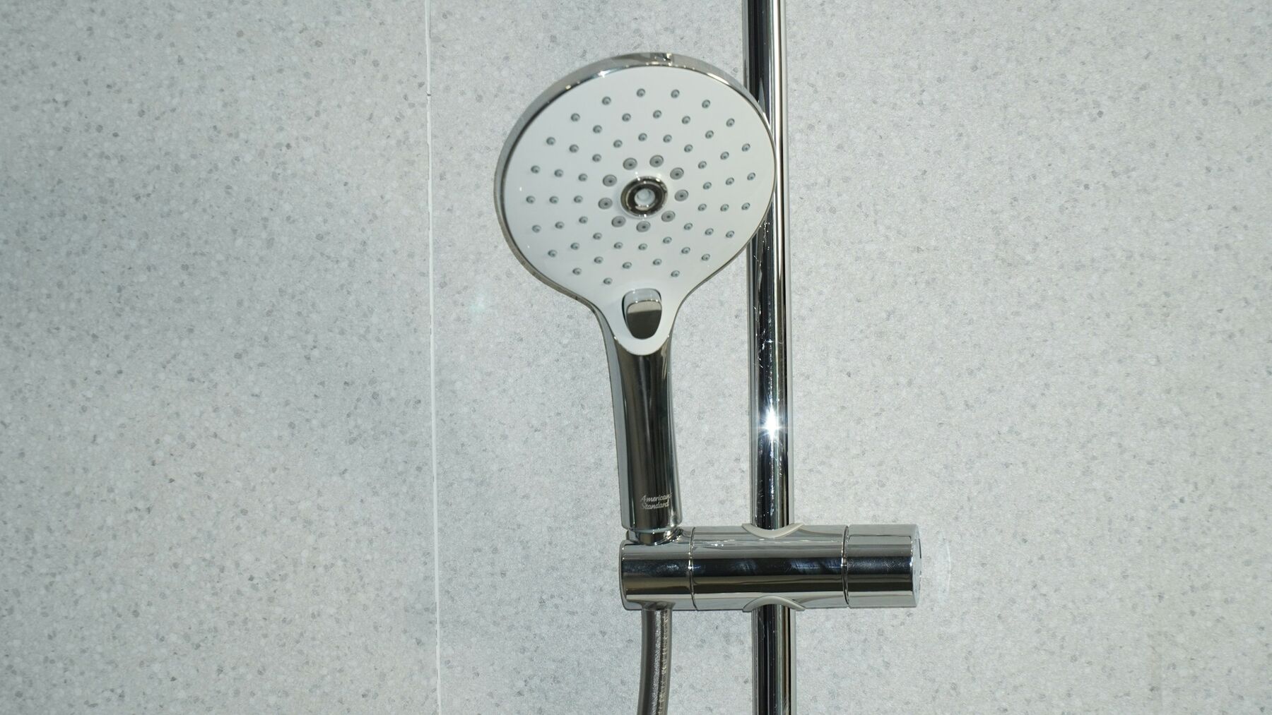A chrome hand shower on a sliding rail against pale wall tiles