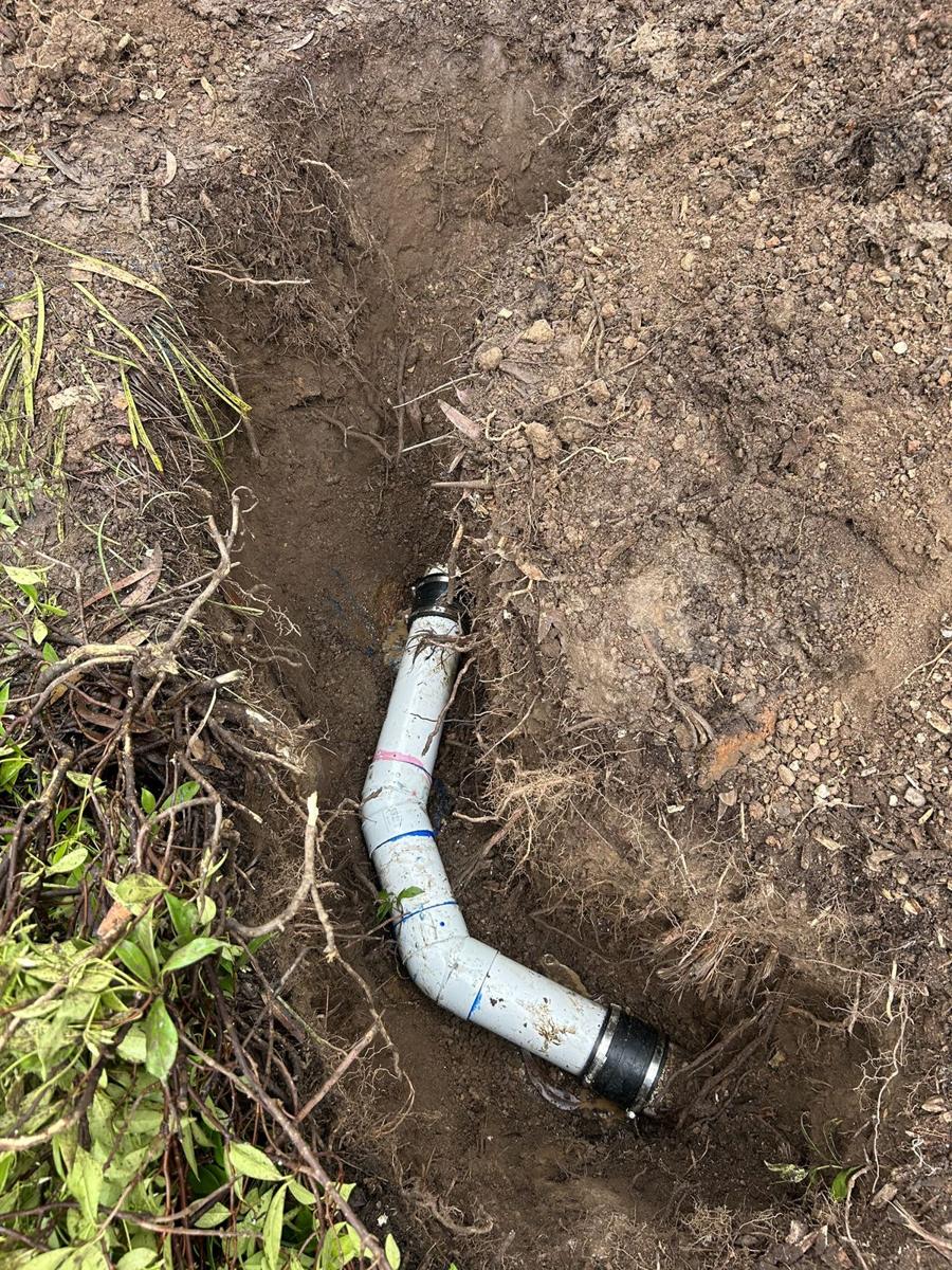 New PVC drain pipe and bend in place in the excavated trench before backfilling